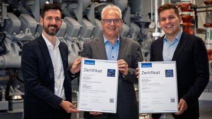 Drei Männer stehen vor einer Netzersatzanlage mit Zertifikaten in den Händen