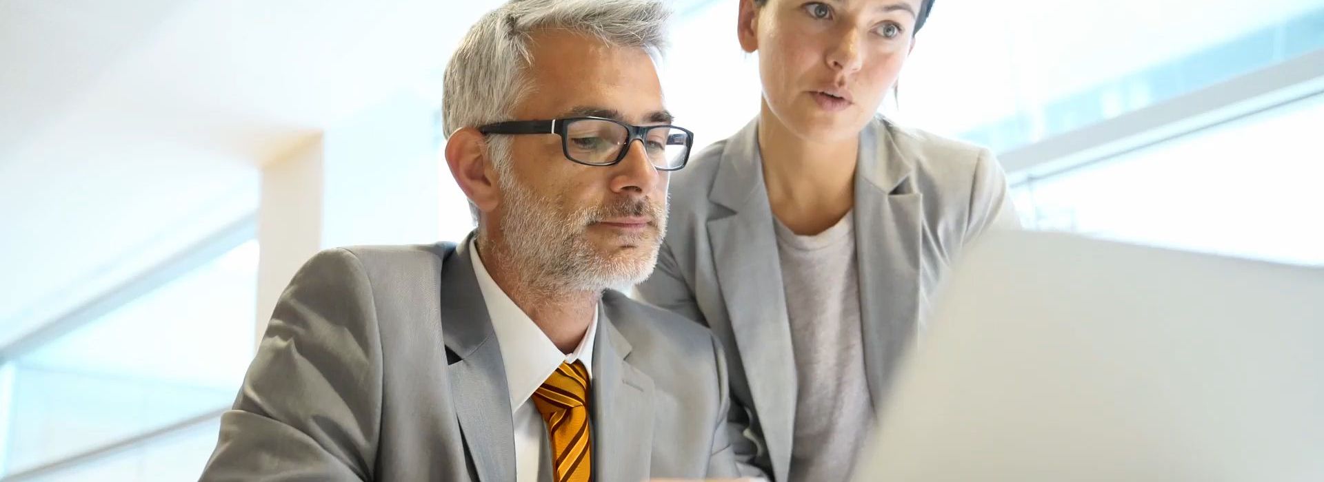 Ein Mann und eine Frau in Business Kleidung vor einem Laptop.