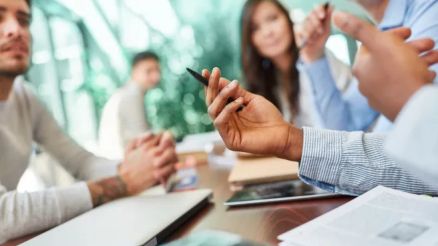 Ein nur verschwommen sichtbare Gruppe von Menschen sitze an einem Tisch und diskutiert.